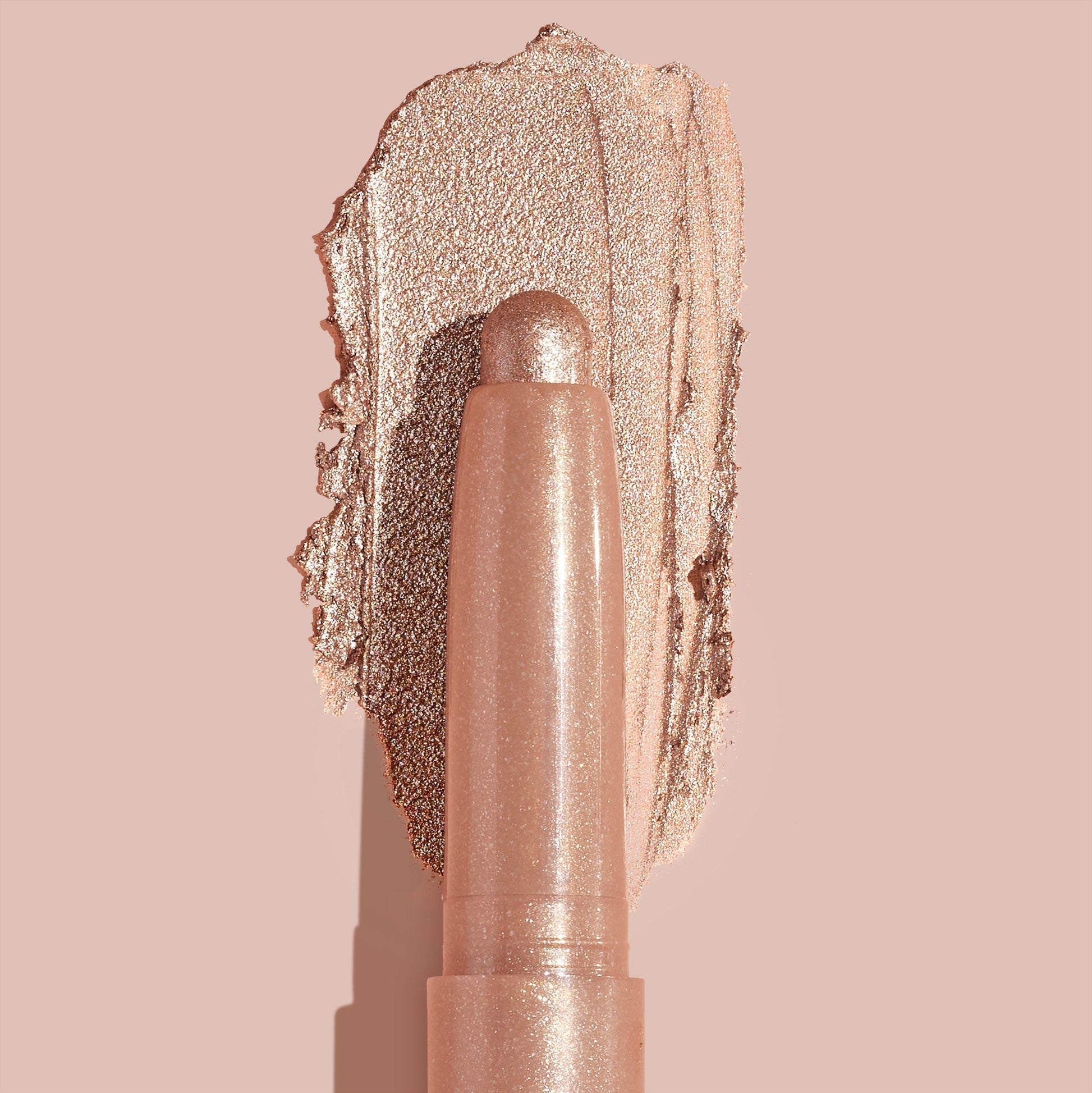 Socialite ColourPop Shadow Stix glides a metallic champagne‑rose swipe across a nude backdrop, twist‑up cream eyeshadow stick shown close up to highlight smooth, blendable texture and high‑shine shimmer for quick eyelid application.