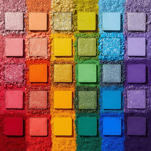 Fade Into Hue shadow palette displays 30 square pans in a rainbow grid - matte, shimmer, and pressed glitter - set on crushed pigment in a deconstructed flat lay; a vibrant ColourPop Shadow Palette.