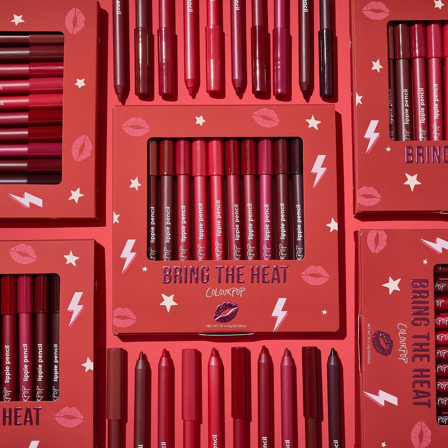 ColourPop Bring The Heat Lippie Pencil set arranged in a flat lay, showcasing creamy lip liners in reds, pinks, and berry tones; boxed and loose pencils surround the main kit on a red background with lips, stars, and lightning graphics.