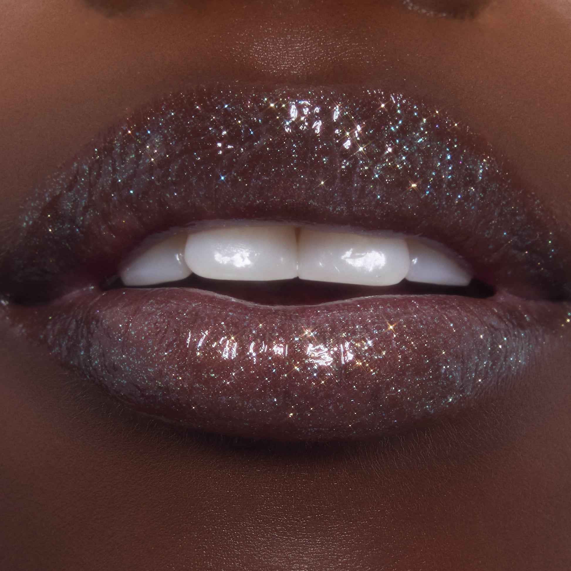 Lips wearing ColourPop Ultra Glossy Lip in Ogre, catching light with multi-dimensional shimmer and glassy shine as teeth gently show; studio macro highlights the deep plum base packed with fine glitter.