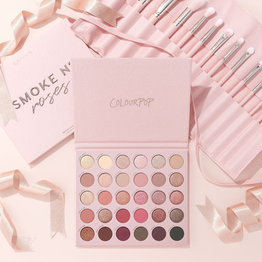 Total Smokeshow ColourPop Shadow Palette & Brush Set displaying rows of rosy neutrals and shimmering tones beside a pink roll of white‑tipped brushes, styled on a soft blush backdrop with satin ribbons.